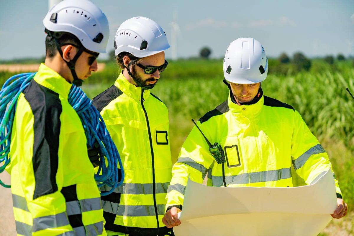 Engineers in safety clothing reviewing construction plans outdoors on a clear day